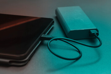 Digital tablet is connected to a portable power bank via a USB cable on a dark surface.