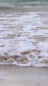 Vertical View of Foamy White Ocean Waves Crashing on Sandy Shore