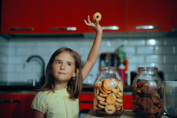 Little Girl Takes a Cookie Out of the Cookie Jar for Snacking. Naughty kid taking desserts from the jar instead of eating lunch