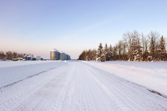 Plowed country road at the farm with granaries in winter.