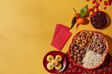 Obraz premium Chinese New Year flat lay with traditional snacks, red envelopes and firecrackers arranged on warm yellow background, designed for graphic and advertising use