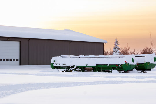 Spirit River, Alberta, Canada - December 27, 2025: John Deere green 635D Header - Draper is parked in the farm yard under high snow after heavy snowfall, orange sunset light and frosty winter.