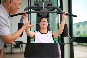 A trainer assisting a young man with down syndrome as he exercises on a weight machine at the gym