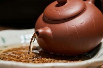A terracotta teapot pouring tea into a ceramic dish, showcasing traditional tea preparation.