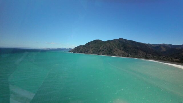 Helicopter cockpit view flying above turquoise ocean coastline