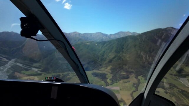 Helicopter pilot side cockpit view over valley and mountains