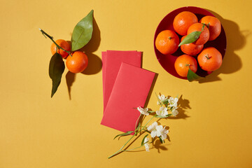 Lunar New Year flat lay scene with red envelopes, lucky fruits and floral accents on yellow...