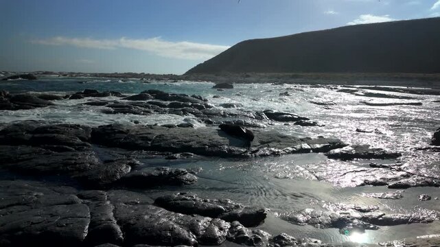 Sun glare on rocky shoreline with waves and distant headland