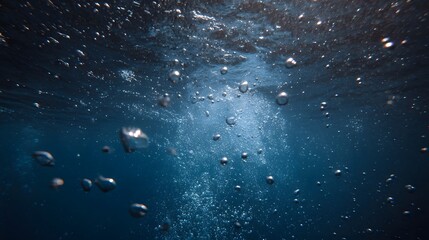 Underwater view of numerous air bubbles rising from the deep blue ocean depths towards the shimmering surface