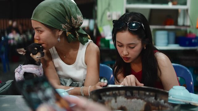 Two women with a chihuahua dog eating moo krata at night