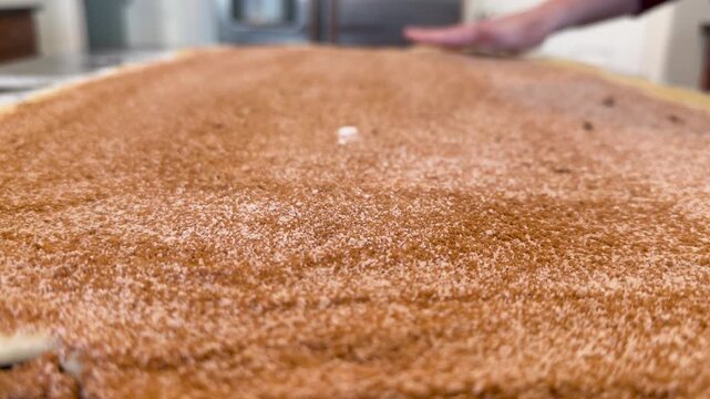 Spreading CInnamon Sugar Evenly Across Cinnamon Roll Dough on Countertop