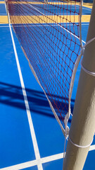 Outdoor Badminton Court with Blue Playing Surface, White Line Markings and Net Casting Pole Shadows in Daylight