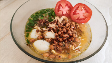 Indonesian chicken soup Soto Ayam with quail eggs and vegetables in glass bowl.