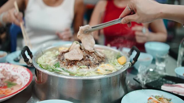 People grilling pork on a traditional thai mookata barbecue pan