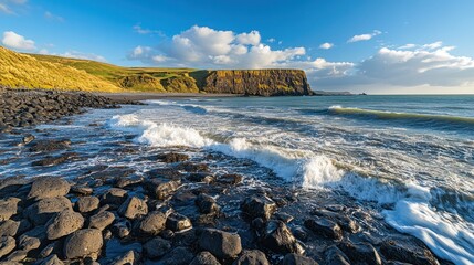 Dramatic rocky coastline with crashing waves under a vibrant blue sky with fluffy clouds, showcasing rugged cliffs and dark, wet stones.