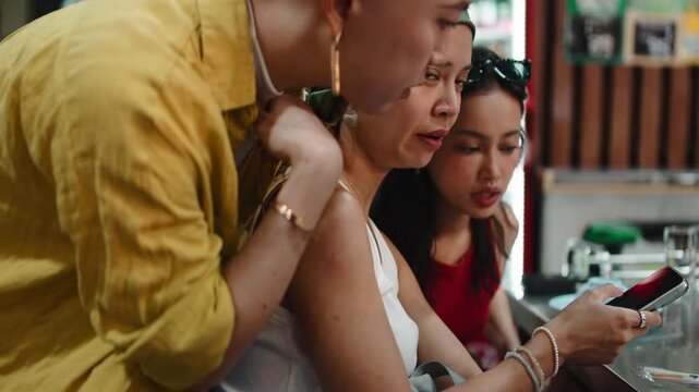Three young friends using a smartphone at a restaurant