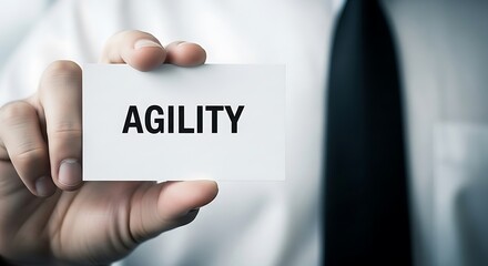 Businessman holding a white business card displaying the bold capitalized word agility concept promoting adaptive management and quick response strategies in corporate settings.