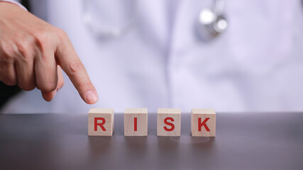 Doctor pointing clinical hand at wooden block showing risk management concept with serious and professional emotion