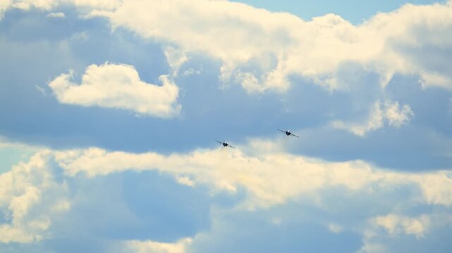 Two military fighter jets fly through a bright cloudy sky in loose formation, leaving subtle trails as they move together across open airspace against bright clouds. POV