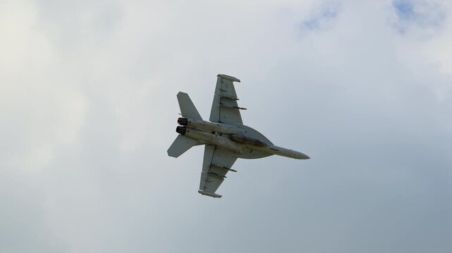 Military fighter jet fly overhead against a blue sky with stormy clouds, creating a dynamic aviation scene with airbase infrastructure. Bottom view