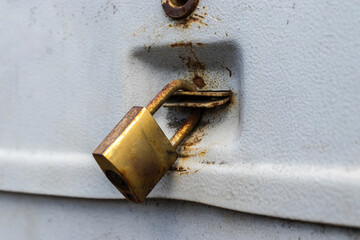 Close-up of a weathered, rusty golden padlock securing a white textured metal surface. A symbol of security, privacy, decay, and the passage of time.