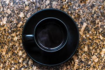 Top-down view of a black coffee cup on a speckled granite with water drops. This minimalist and modern image evokes the feeling of a morning routine, a moment of focus, or a simple coffee break