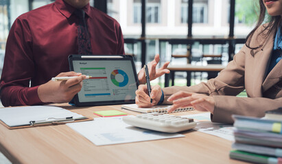 Financial Strategy: Close-up of two business professionals engaged in an analytical discussion. Focused on a digital tablet showcasing charts and graphs.