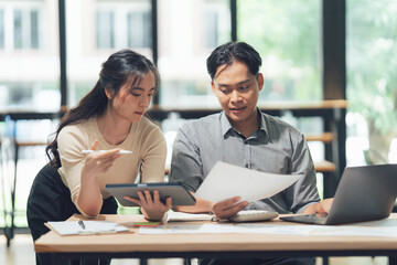 Collaborative Review: Two professionals engage in a focused discussion over documents, with one pointing at a tablet, representing shared analysis, strategy.