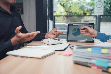 Discussing business data: Two individuals engaged in a dynamic discussion around a desk adorned with a tablet displaying key data, emphasizing collaborative work