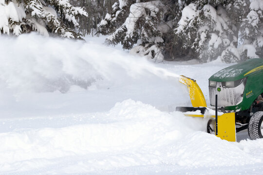 Spirit River, Alberta, Canada - December 27, 2025: John Deere compact tractor with a snowblower is plowing snow cleaning the driveway in the rural area. Snowy day in cold winter.