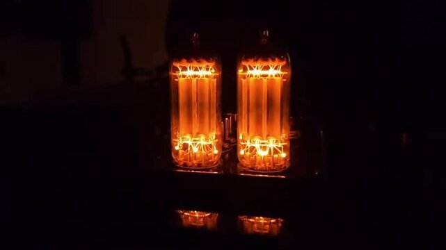 Two lit vacuum tubes with orange glow in a dark room. Reflections are visible below