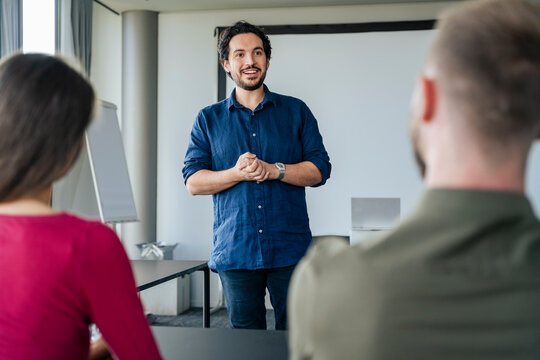 Smiling young businessman giving presentation to colleagues sitting at desk in office