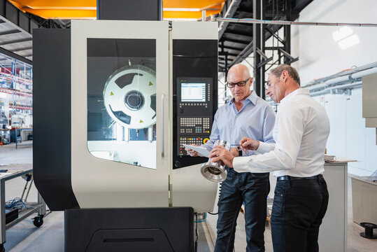Employees discussing engineering process at machine in production hall