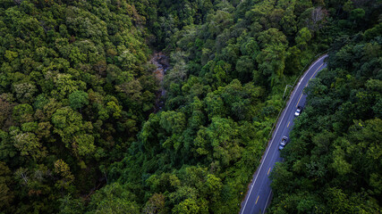 Drone view of an intelligent electric vehicle navigating a scenic road through lush forest, representing next generation mobility solutions.