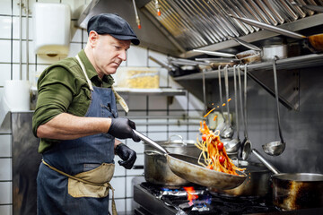 Chef cooking pasta in restaurant kitchen with apron and gloves