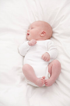Baby lying on white bed in sleepwear indoors