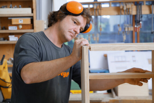 Carpenter working on wood furniture in a workshop wearing ear protection