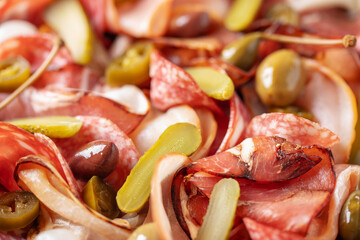 Meat charcuterie plate with different sausage and bacon and pickled vegetables.