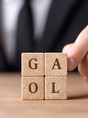 Event of hand placing wooden blocks spelling goal indoor setting close-up view conceptual focus on achievement
