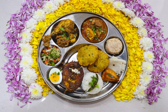 Traditional Indian non-veg thali with kombdi vade, chicken fry, mutton curry, fish fry, boiled egg, rice, sheera, salad, dhokla and samosa.