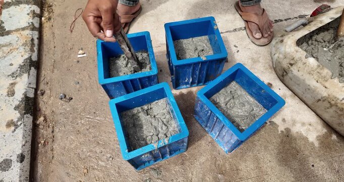 close up of a worker tamping wet concrete into blue plastic cube molds for compressive strength testing