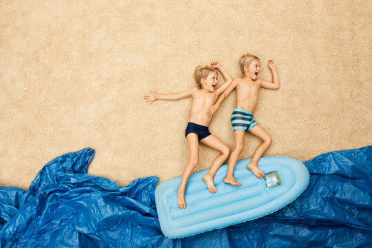 Children playing on inflatable raft on artificial beach scene in studio