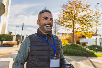 Smiling professional outdoors in casual attire with badge and documents