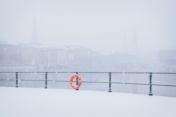 Snowy winter city view of Binnenalster Hamburg with lifebuoy and railing