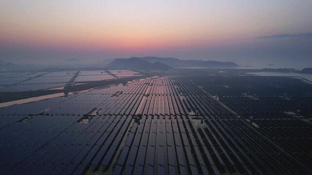Solar panel arrays on tidal flats at dawn with distant misty mountains and coastal wetlands