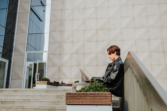 Serious student sitting outdoors on school yard studying with laptop