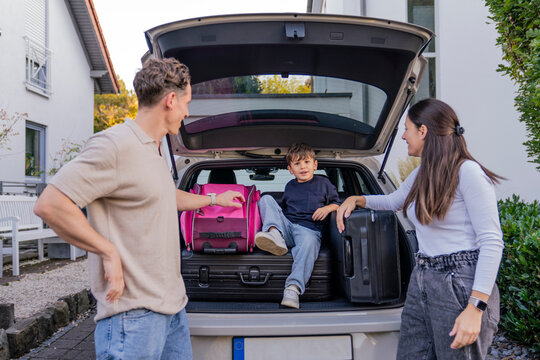 Family preparing for vacation packing suitcases into electric car