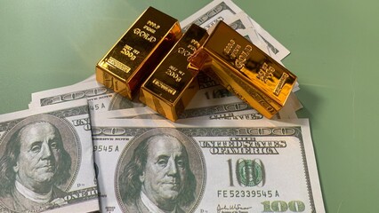 Gold bars placed on multiple US hundred dollar bills, symbolizing wealth, investment, and financial, concept photo