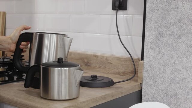 Close up of stainless steel electric kettle unplugged from wall socket on wooden kitchen countertop, representing hot drink preparation, home appliances and daily routine.