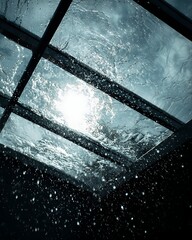 Dramatic rain falling on skylight glass roof with bright sun glare